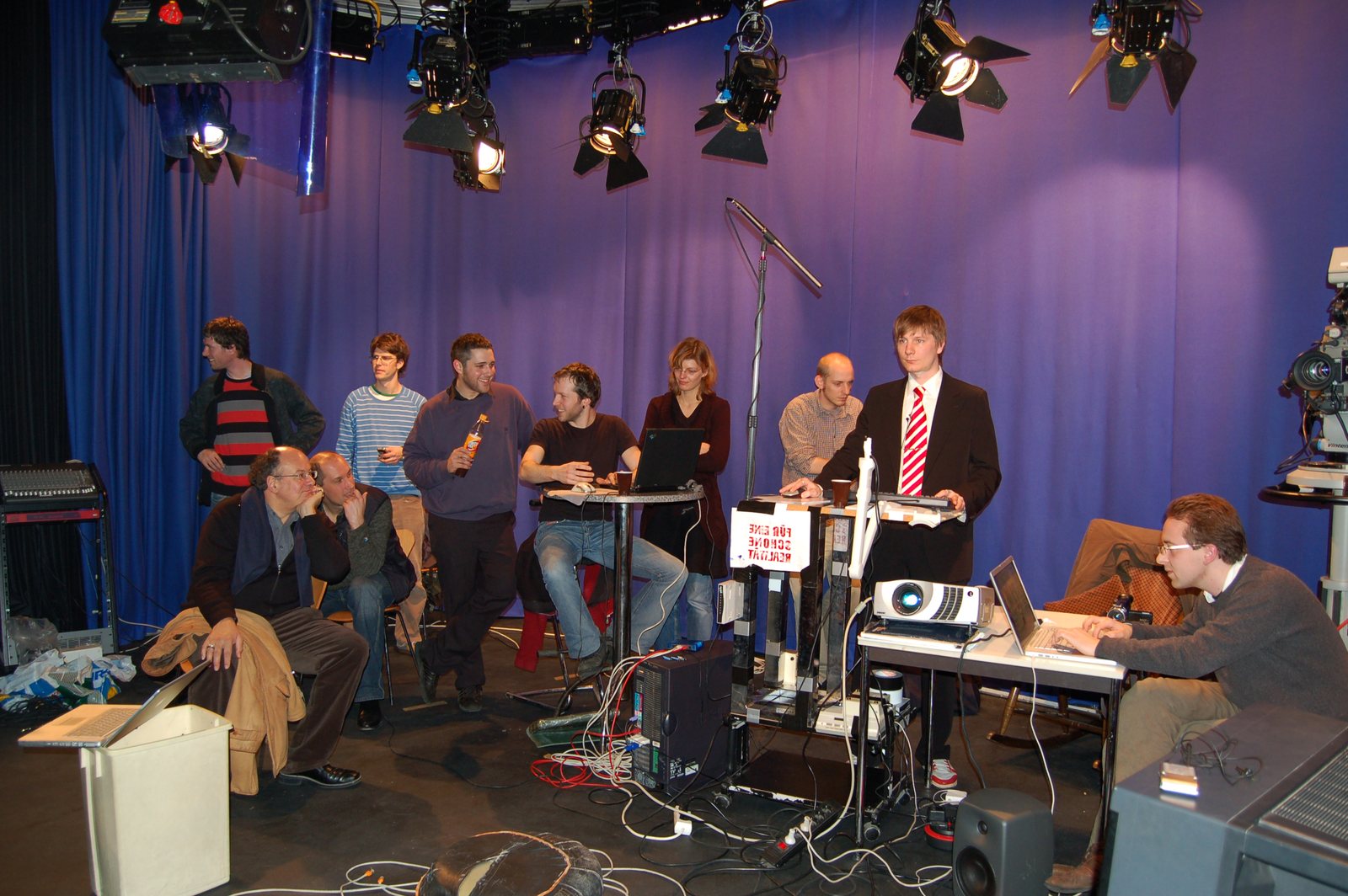 The bluebox studio in Cologne — Kuhlmann in a business look at the command desk with an 'I buy...' sign, the team and cameras around